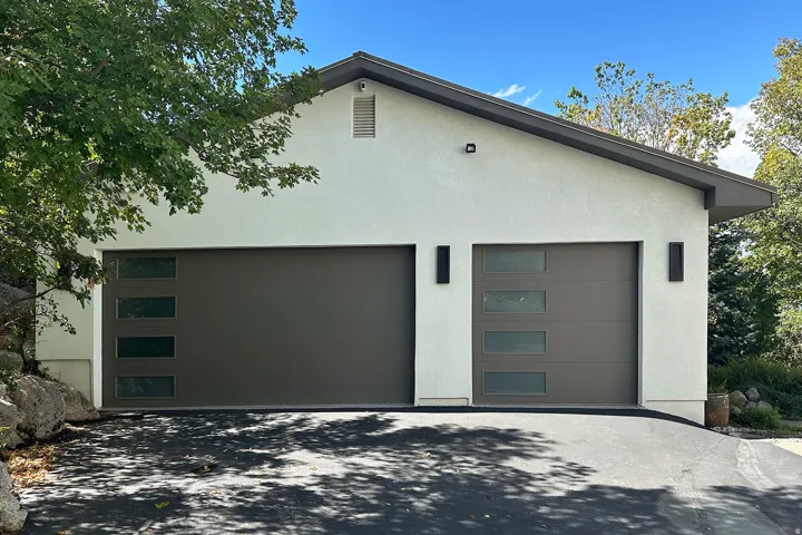 Stucco exterior featuring dual garage doors with frosted glass panels, an asphalt driveway, and exterior lighting fixtures