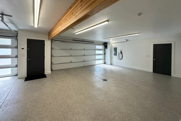 Spacious two-car garage with an epoxy-coated concrete floor, modern overhead lighting, and a visible wood beam