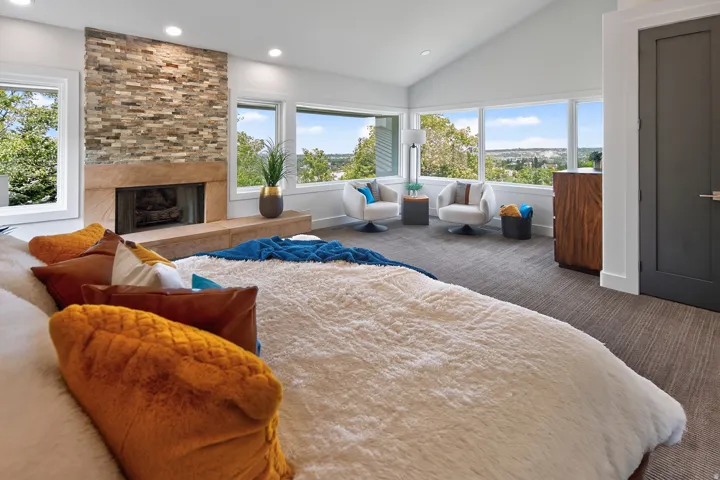 Vaulted ceilings, a stacked stone fireplace with a substantial hearth, large windows, dark panel door, and textured carpeting