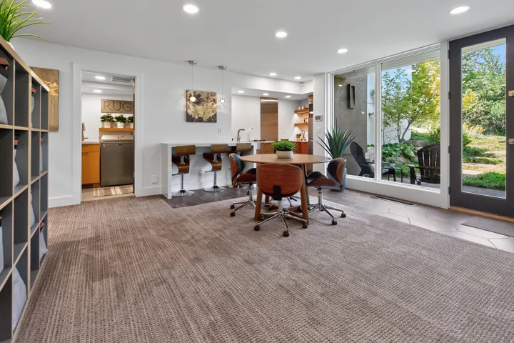 Recessed lighting illuminates the open-concept space, featuring a built-in shelving unit, a breakfast bar, and a dining area with a round table