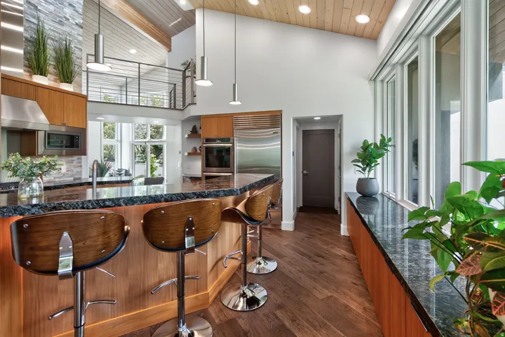 Vaulted wood-paneled ceiling with recessed lighting, wood-finish flooring, stainless steel appliances, large windows, and a stone-clad accent wall