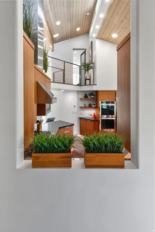 Vaulted wood-paneled ceiling with recessed lighting, wood-finish cabinetry, stainless steel appliances, and a metal cable railing system
