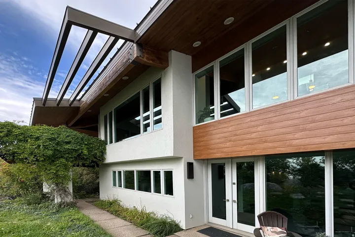 Modern exterior featuring large windows, wood-finish siding, white stucco, and a pergola