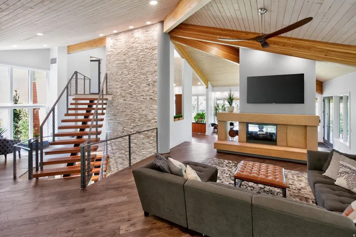 Vaulted wood-paneled ceilings, stone accent wall, open-tread staircase with metal railings, built-in fireplace with hearth, and wood-finish flooring