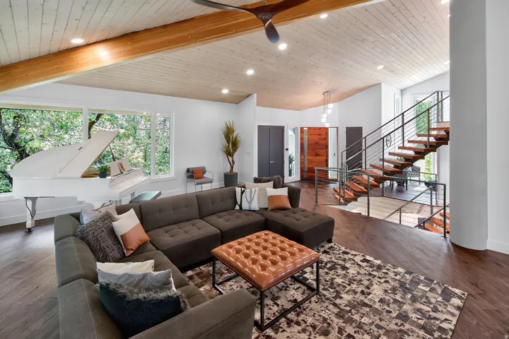 Vaulted wood-paneled ceiling with exposed beam, large picture windows, wood-finish flooring, open-tread staircase with metal railings, and recessed lighting