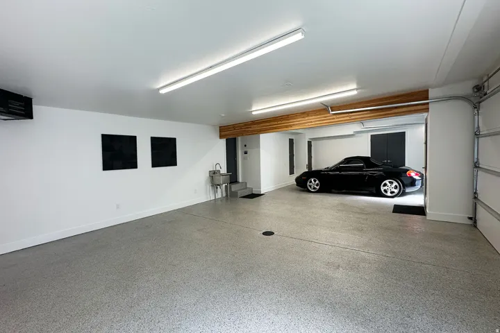 Spacious garage featuring a finished epoxy floor, utility sink, overhead lighting, and white walls