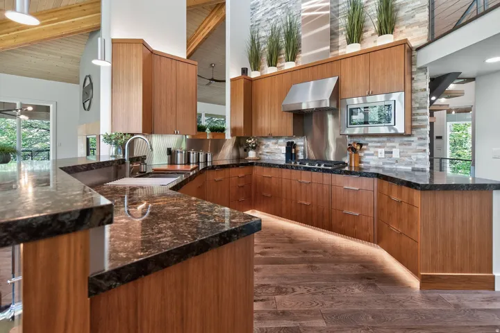 Kitchen featuring dark stone countertops, wood-finish cabinetry, stainless steel appliances, and a stone accent wall