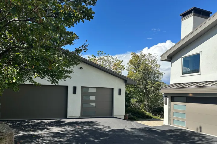 Stucco exterior with a pitched roofline, modern garage doors featuring frosted glass panels, and exterior wall sconces