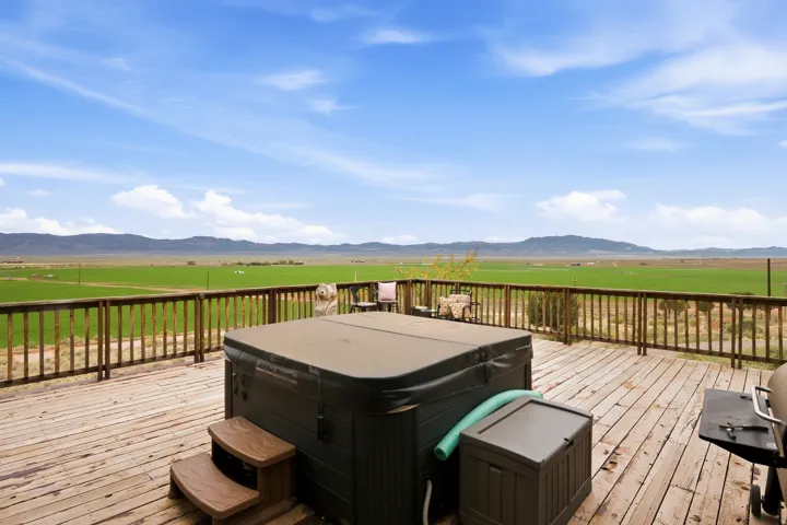 Expansive outdoor deck with wood railing, featuring a hot tub with steps and a wide agricultural landscape with distant mountains