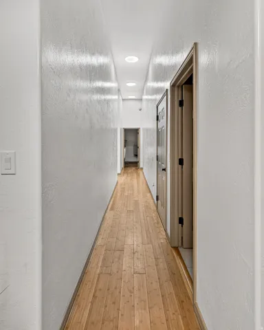 Elongated corridor with wood-finish flooring, recessed ceiling lighting, and textured wall finishes