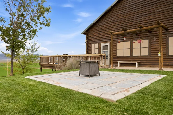 Expansive lawn with a stone paver patio, wood-decked balcony, and a log-cabin style exterior