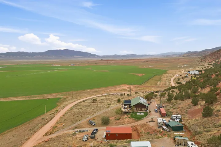 Expansive green fields, mountainous surroundings, residential structure with a green roof, outbuilding with a red exterior, and an additional outbuilding with a green roof