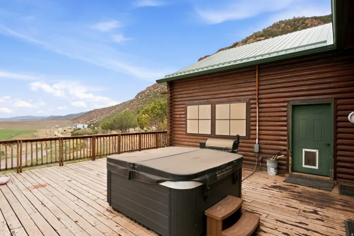 Spacious wooden deck with railing, featuring a hot tub and a log cabin style exterior