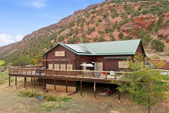 Log-sided residence featuring a green metal roof, a wrap-around wood deck, and solar panels