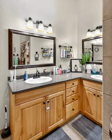 Dual vanity with wood-finish cabinetry, solid surface countertops, and framed mirrors