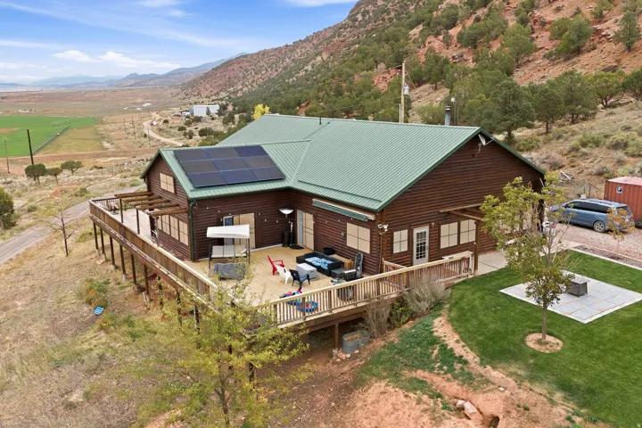 Log-sided exterior with a green metal roof, expansive wrap-around deck, integrated solar panels, and a landscaped lawn with a fire pit area