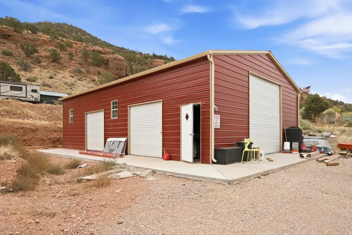 Red metal-sided structure with a gabled roof and multiple roll-up garage doors
