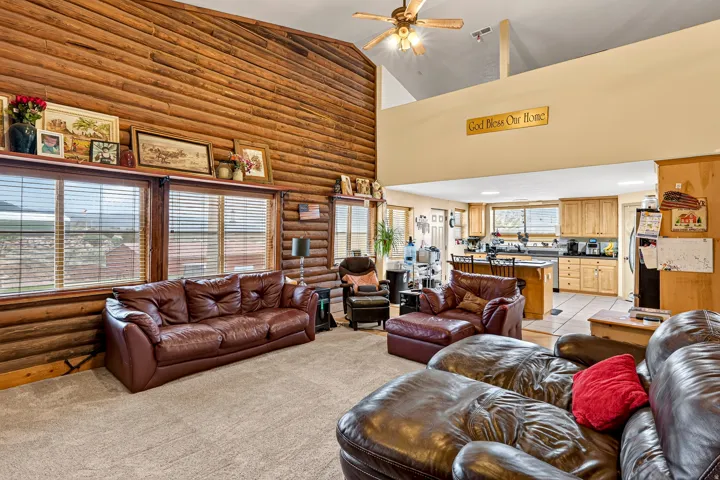 Vaulted ceiling with an exposed wood beam, wood-paneled walls, large windows, and an open-concept kitchen with wood cabinetry