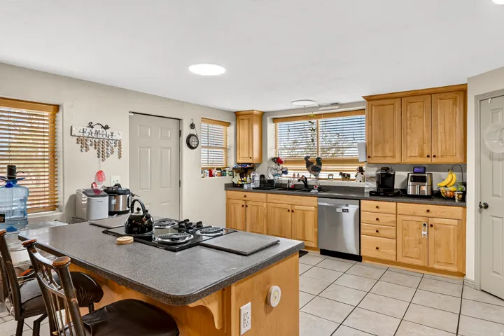 Kitchen featuring light wood cabinetry, a central island with an integrated cooktop, a stainless steel dishwasher, and tiled flooring