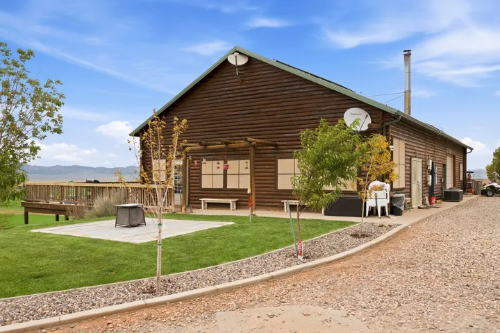 Log cabin exterior with a durable green roof, an expansive outdoor deck, and a gravel driveway