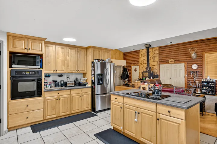 Kitchen featuring wood cabinetry, stainless steel refrigerator, built-in oven and microwave, and a center island with cooktop