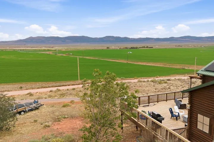 Expansive wooden deck with a slatted railing, surrounded by natural landscaping and distant green fields