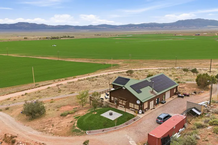 Property featuring a metal roof with solar panels, a brown wood-clad exterior, a gravel driveway, and a partially landscaped yard with a fire pit