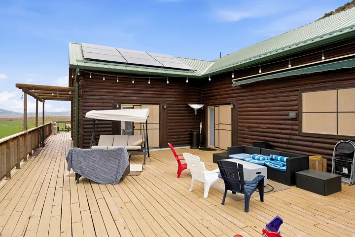 Expansive outdoor decking, log siding, solar panel array, green metal roofing, and a covered porch