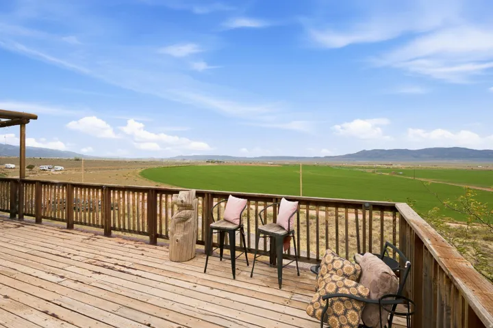 Expansive wood-finish deck with wood railing, featuring distant green fields and mountain backdrop