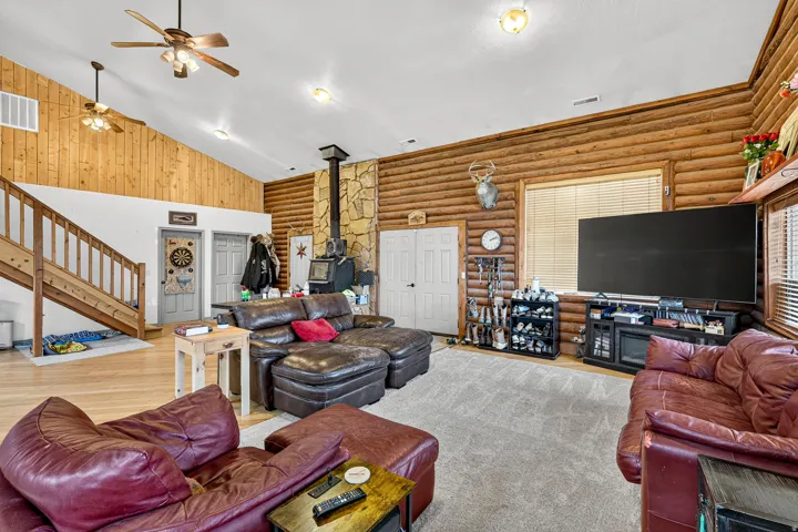 Vaulted ceiling with wood paneling, wood-finish walls, wood staircase, and stone-clad wood-burning stove with a metal flue