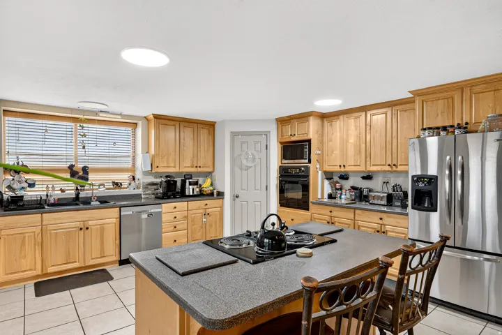 Kitchen with wood cabinetry, stainless steel appliances, a center island with cooktop, and two skylights