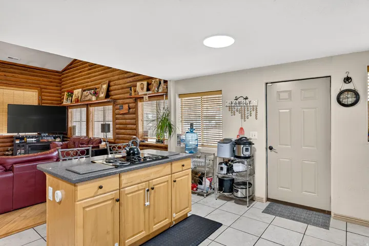 Wood-paneled living area with vaulted ceilings, a kitchen island with built-in cooktop, and light-colored tile flooring