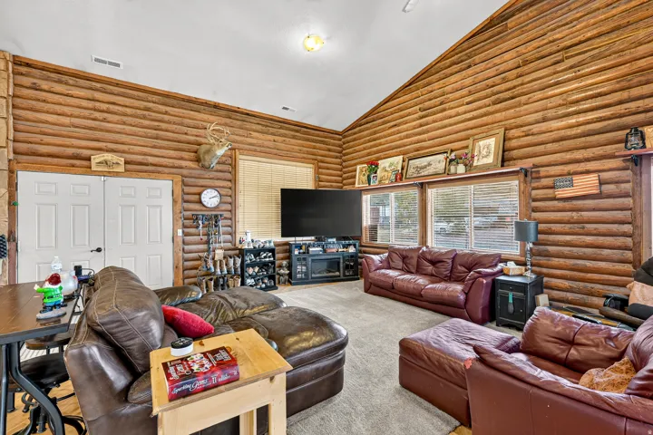 Vaulted ceiling, log walls, neutral carpeting, double pane windows, and a built-in media console with an electric fireplace