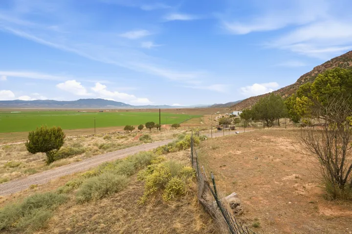 Expansive rural landscape featuring a gravel road, distant green fields, mature trees, and mountainous terrain
