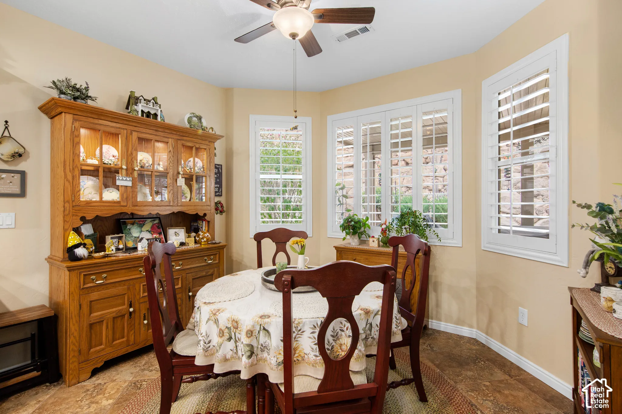 Bay window with plantation shutters, ceiling fan with integrated lighting, wood-finish flooring, and light-toned wall paint