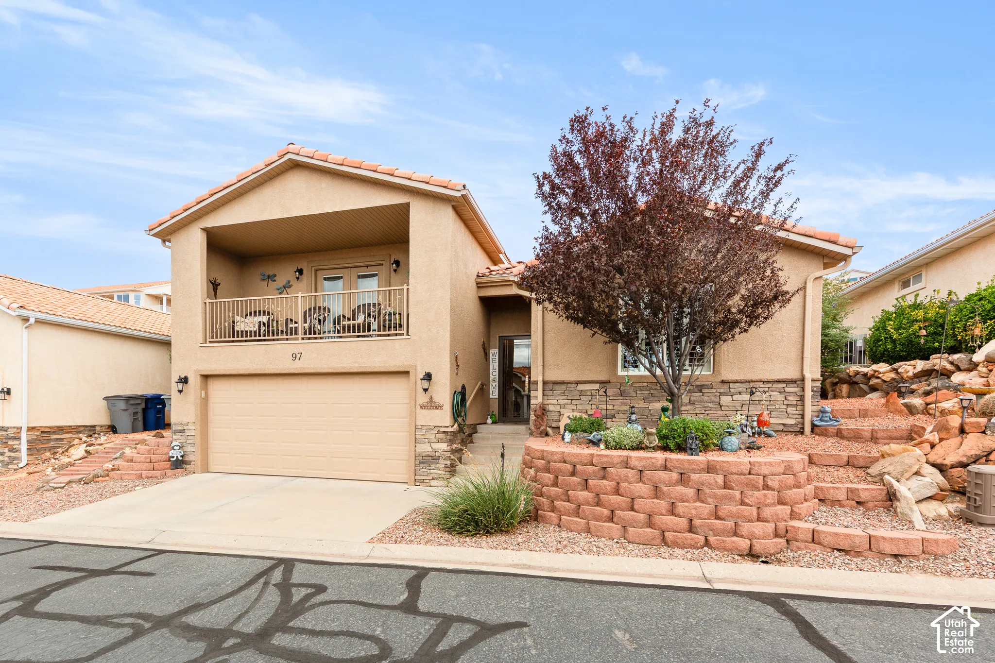 Stucco exterior with stone accenting, an integrated garage, a second-story covered balcony, and terraced landscaping