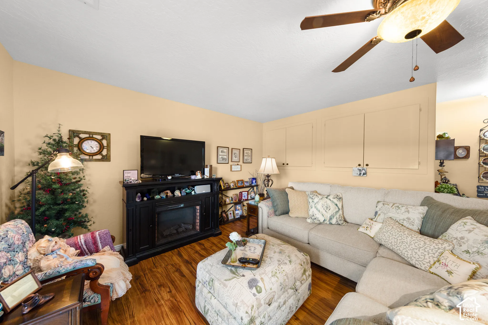Wood-finish flooring throughout, electric fireplace, ceiling fan with integrated lighting, and built-in wall cabinetry