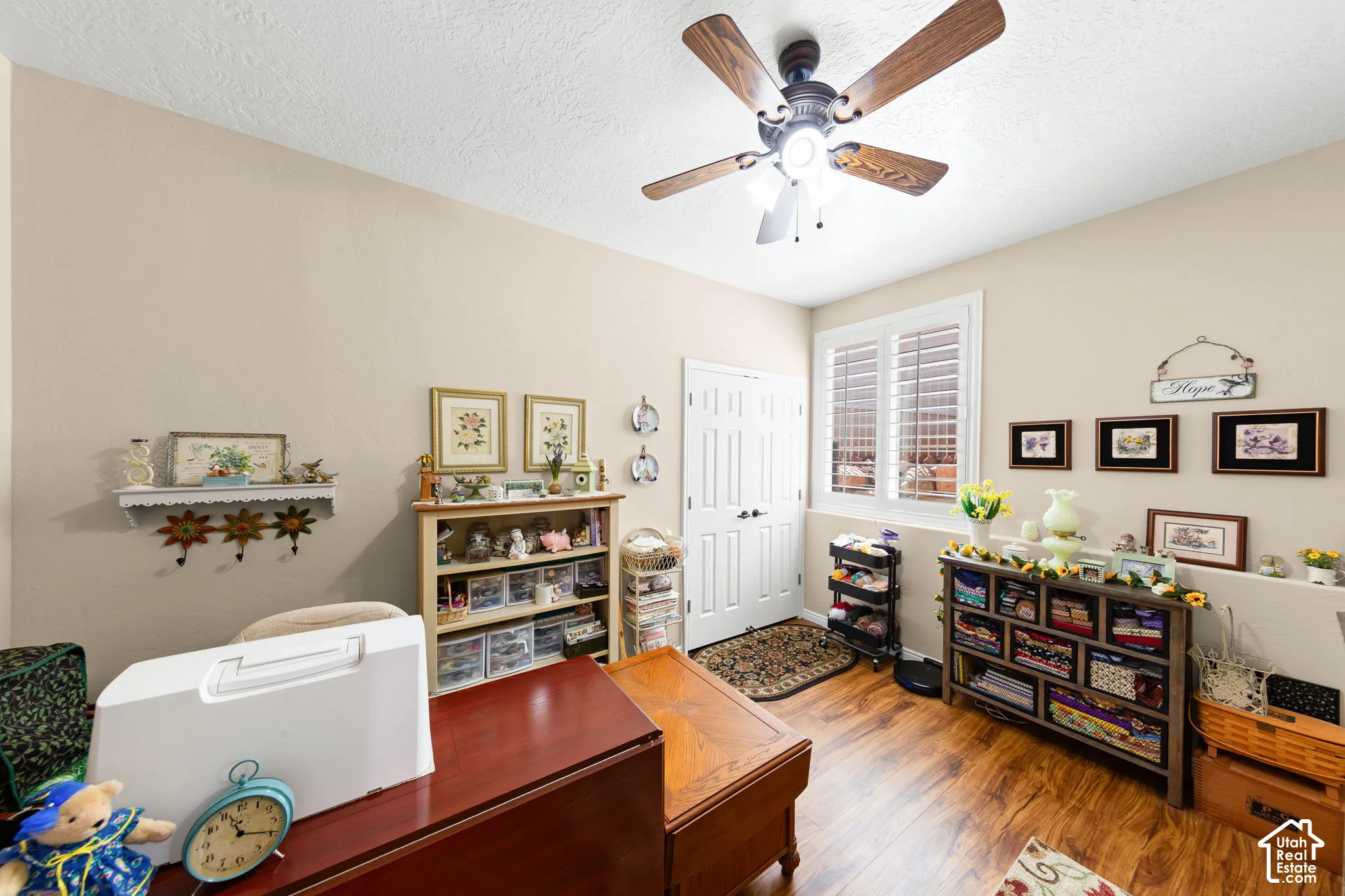 Wood-finish flooring, ceiling fan with light fixture, white window shutters, and a white paneled door