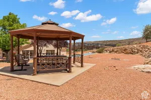 Hexagonal gazebo with a metal roof on a concrete pad, surrounded by desert landscaping, rock outcroppings, and mature trees