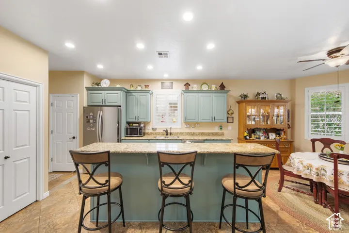 Kitchen featuring a central island with countertop seating, recessed lighting, stainless steel refrigerator, and light blue cabinetry