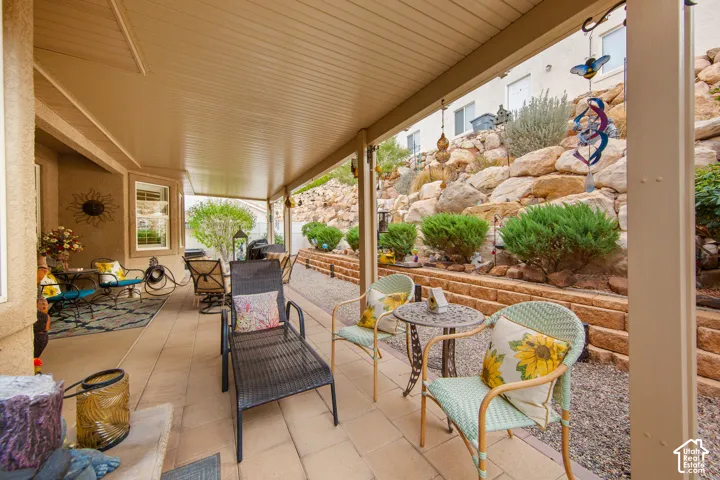 Covered patio featuring paver flooring, a beadboard ceiling, and a tiered rock wall with integrated landscaping
