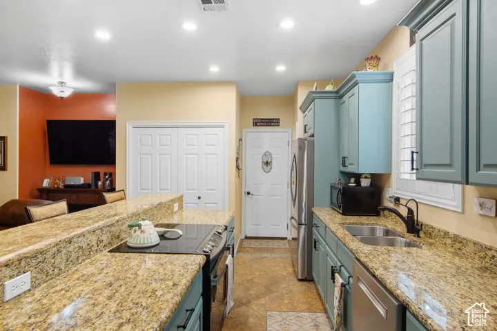 Kitchen featuring granite-style countertops, stainless steel appliances, blue-painted cabinetry, and a double-basin stainless steel sink