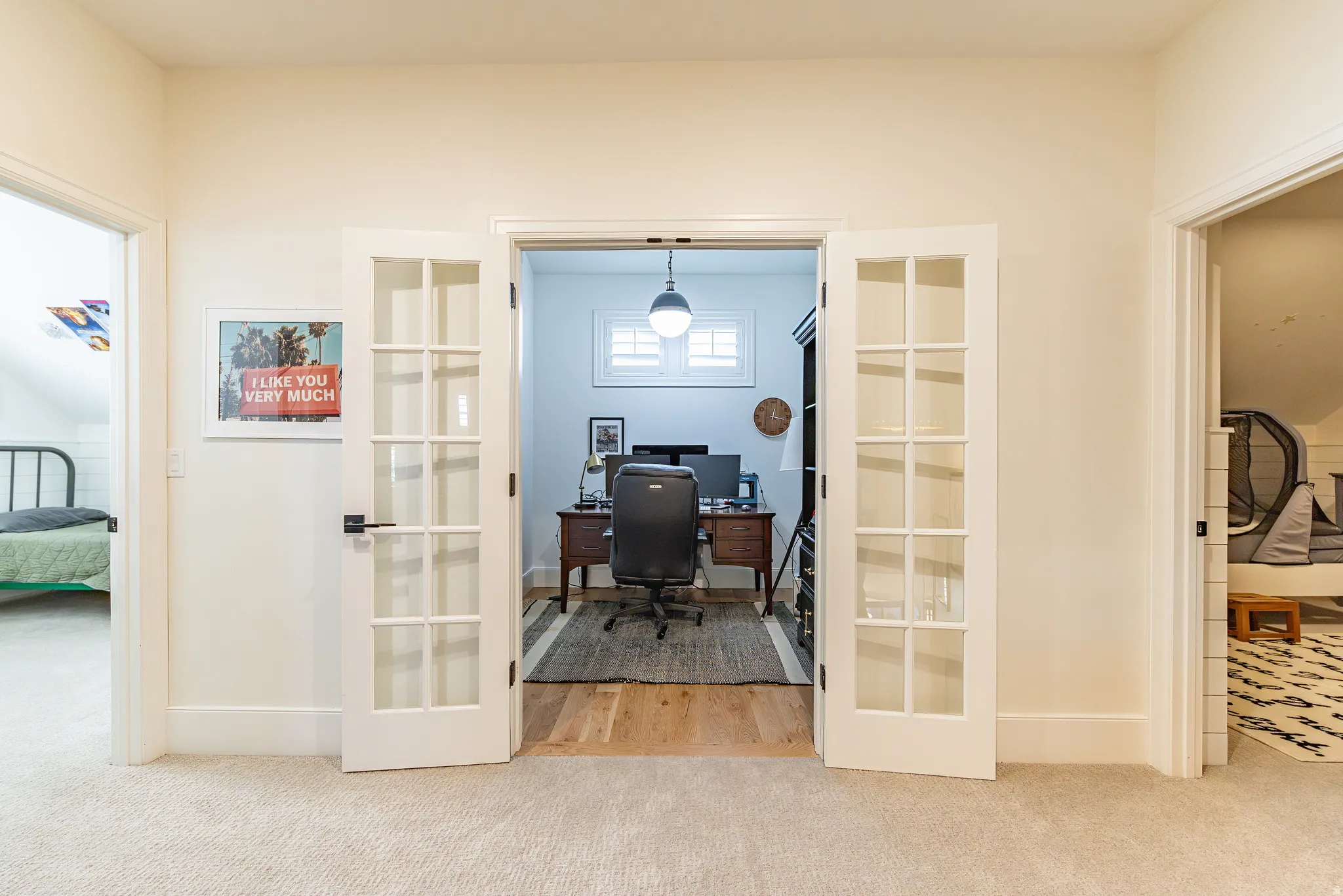 Carpeted hallway leading to a room with wood-finish flooring and French doors