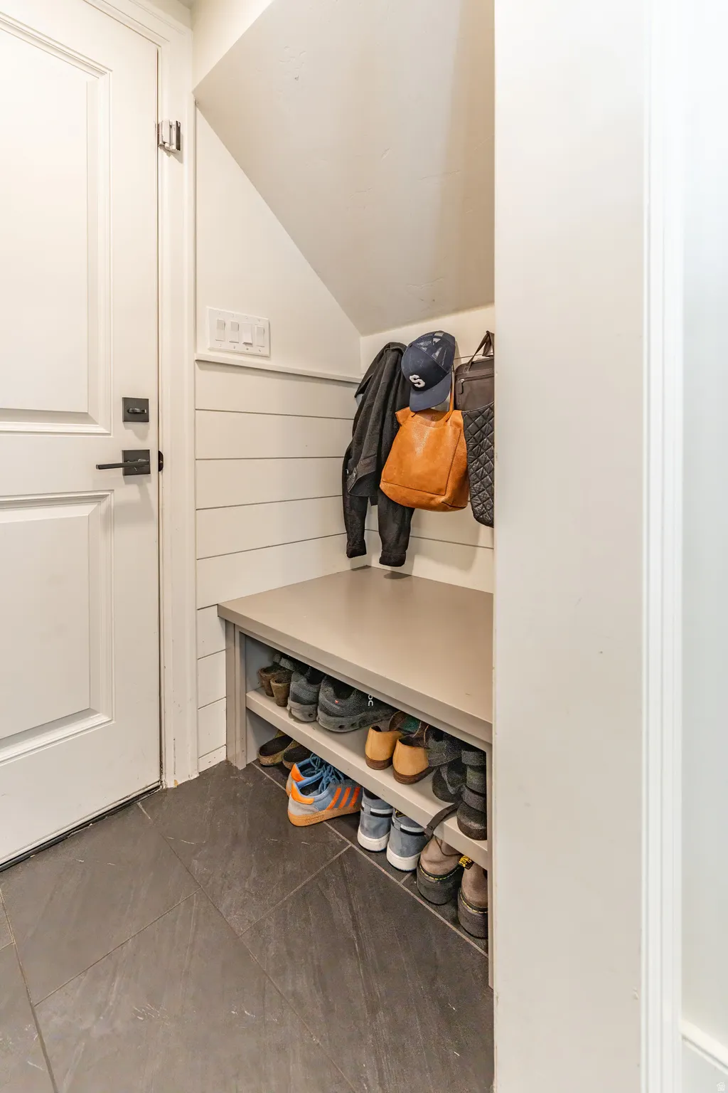 Built-in storage bench with shelving, shiplap wall accent, and slate-finish floor tile