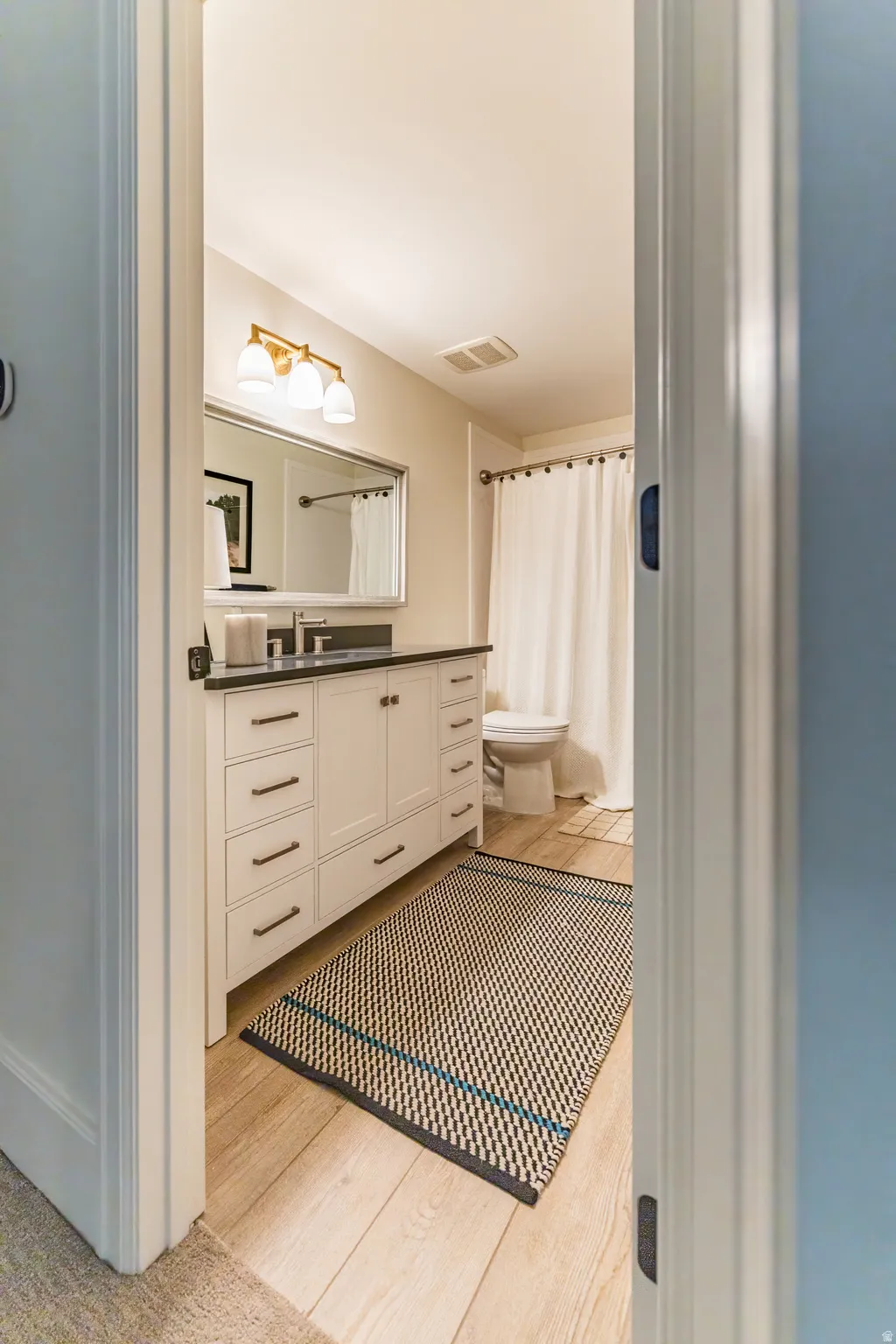 Wood-finish flooring with a white vanity featuring multiple drawers and cabinets