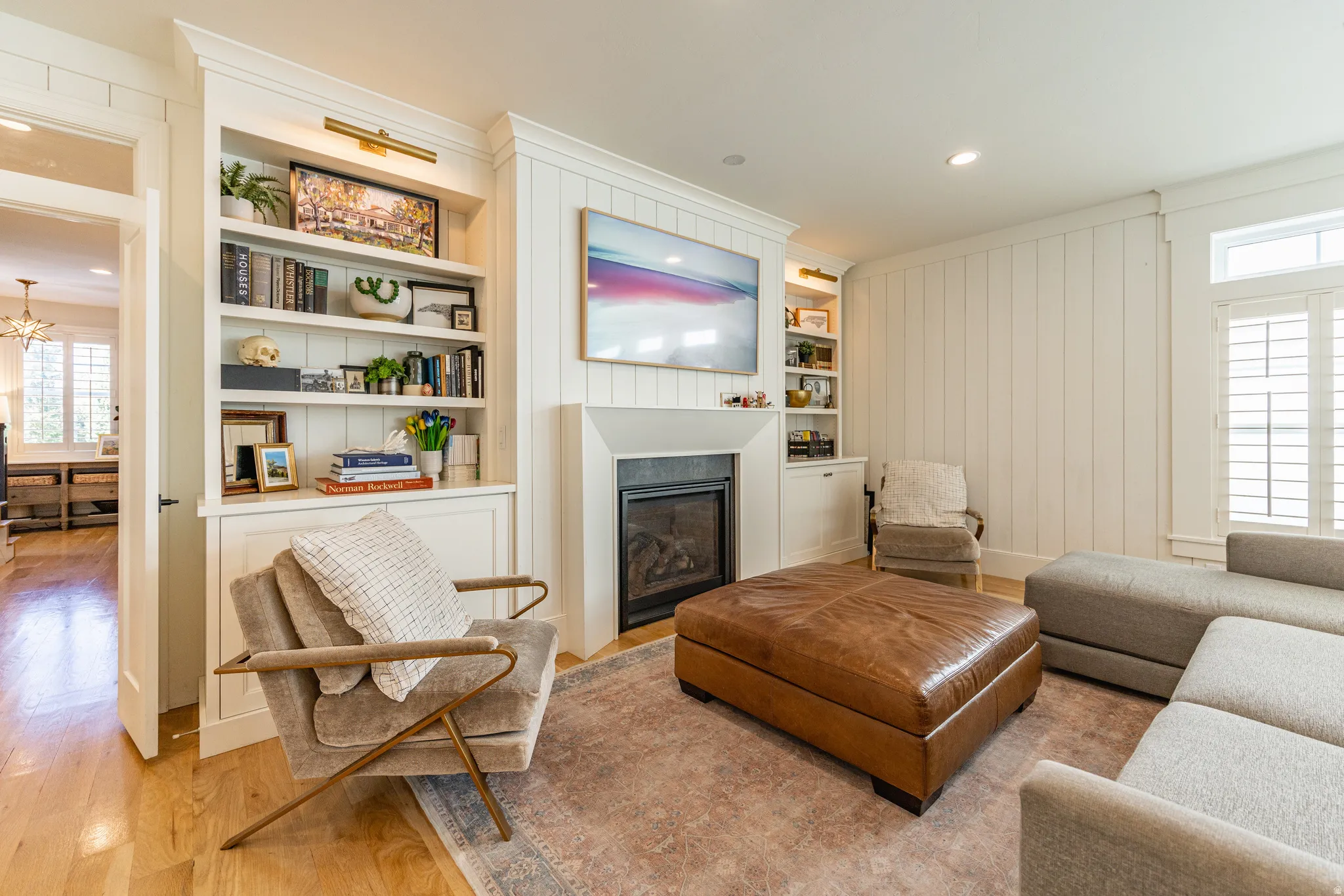 Living space featuring wood-finish flooring, built-in shelving, a fireplace with a stone surround, and shiplap wall detailing