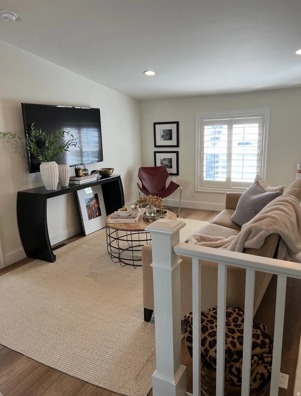 Recessed lighting, wood-finish flooring, white walls, and a window with white louvered shutters