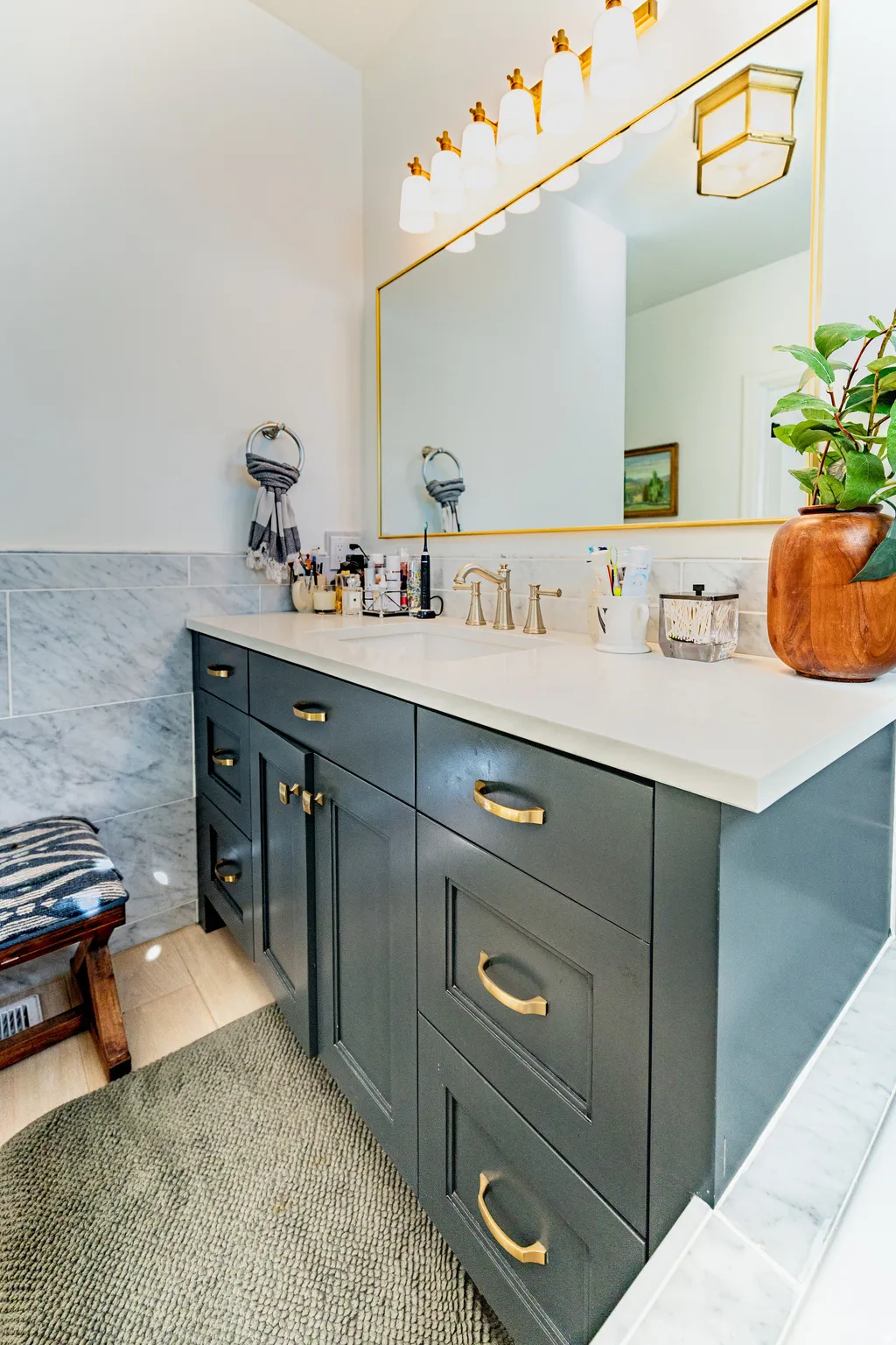 Spacious vanity with grey cabinetry, gold-toned hardware, solid surface countertop, and large framed mirror
