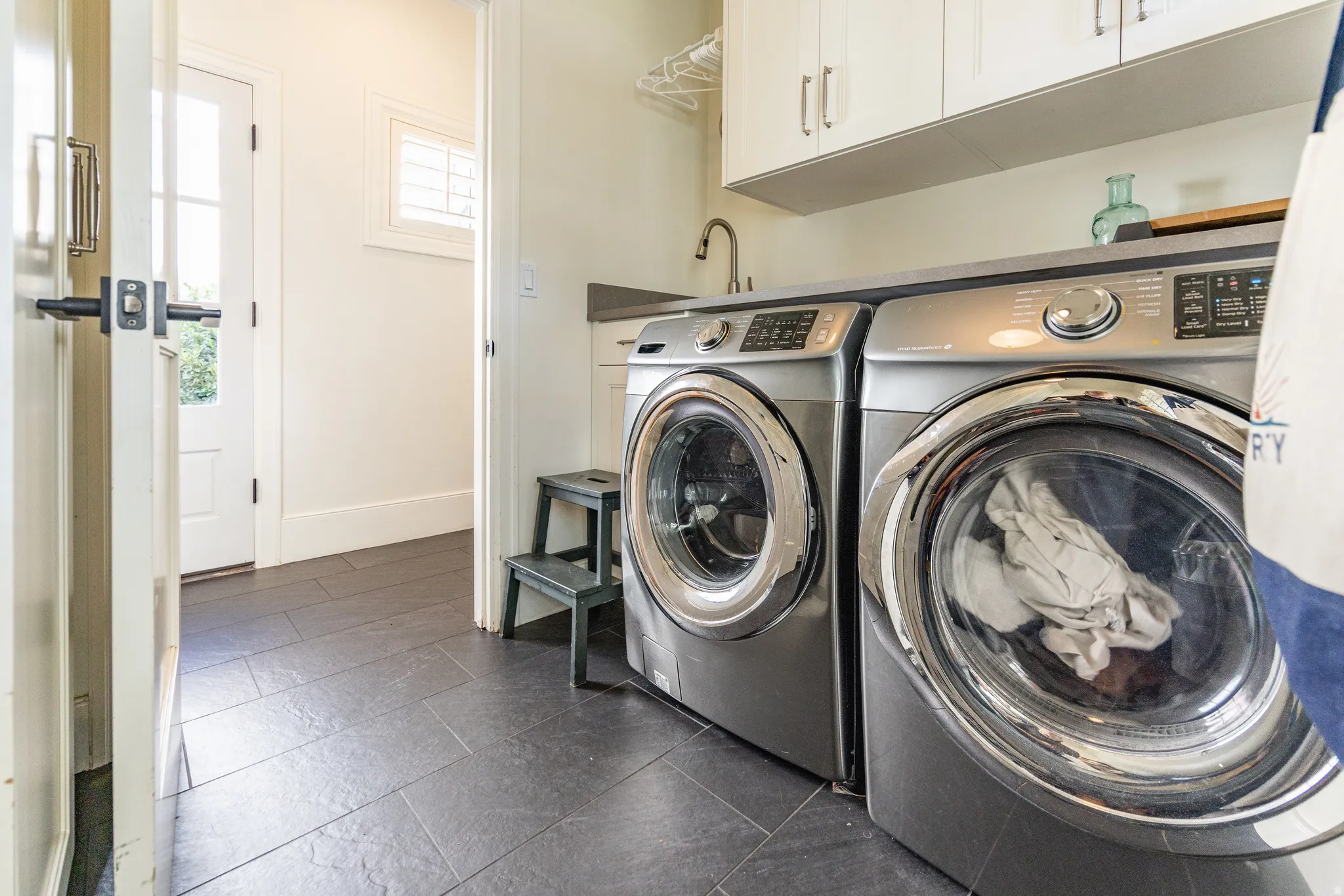 Laundry area featuring a built-in sink, white cabinetry, and dark tile flooring