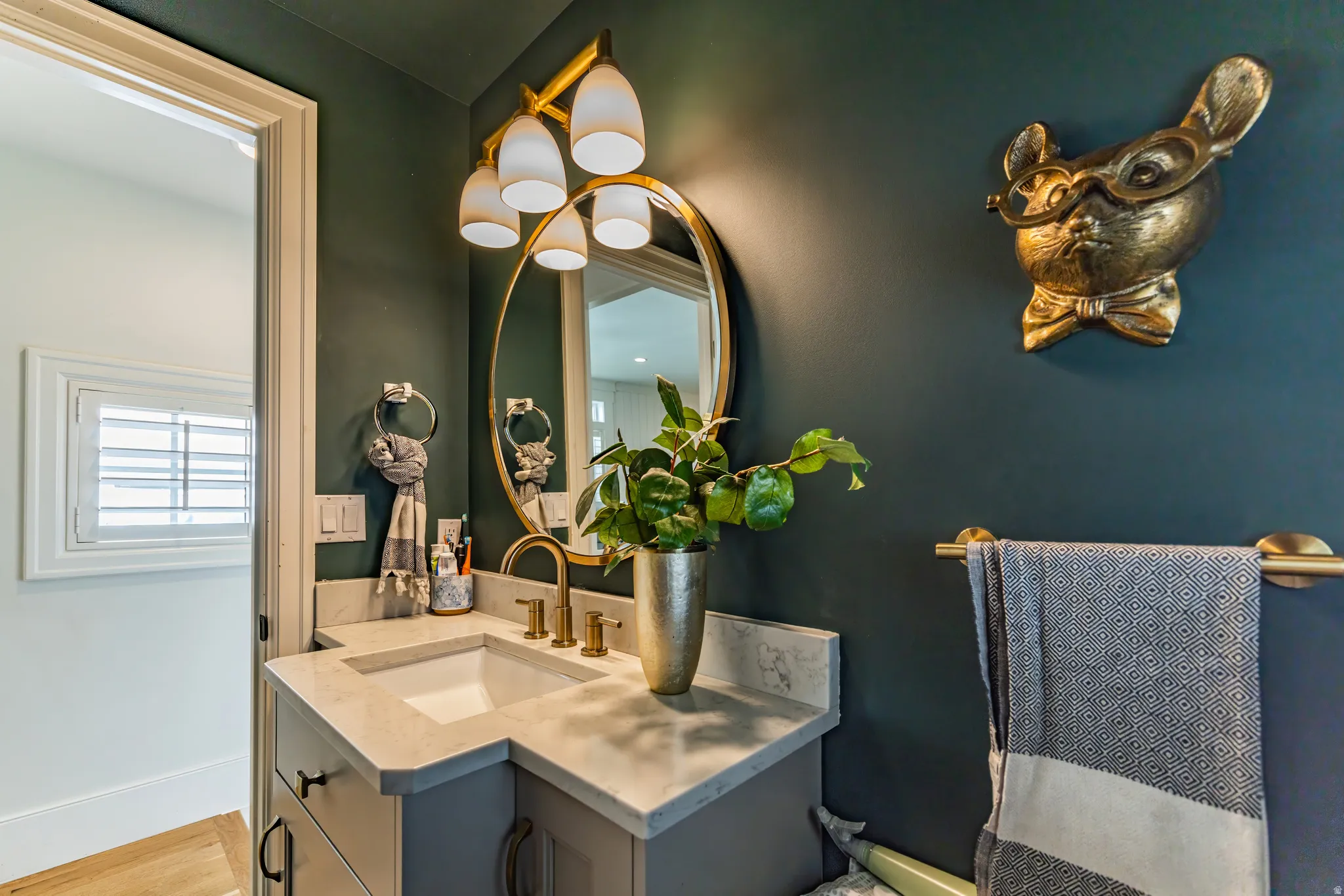 Vanity with a light-colored countertop and integrated sink, gold-finish faucet, and an oval mirror with a gold-tone frame